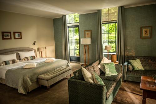 een slaapkamer met een bed en 2 stoelen en een bank bij Koetshuis Landgoed Lauswolt in Beetsterzwaag