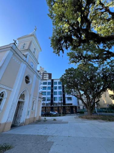 a white building with a clock tower next to a tree at Hotel Valerim Itajaí / Navegantes in Itajaí