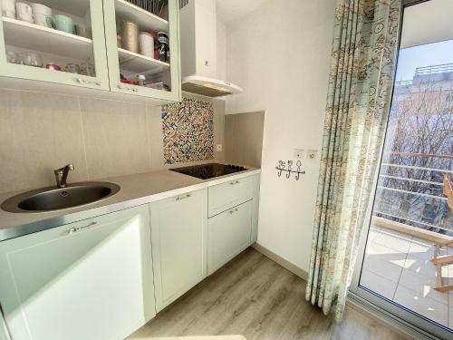 une cuisine avec des armoires blanches, un évier et une fenêtre dans l'établissement A303- Appartement 3 pieces 4 personnes- Le Crystal, à Cagnes-sur-Mer