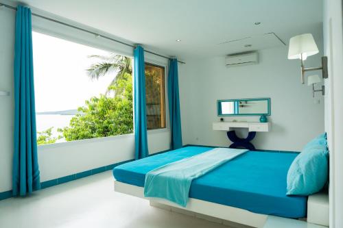 una camera con un letto blu e una grande finestra di villa piscine à louer a DIEGO SUAREZ. MADAGASCAR a Antsiranana