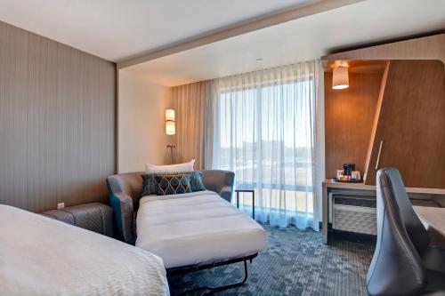 um quarto de hotel com uma cama e uma cadeira e uma janela em Courtyard by Marriott Bentonville Rogers Promenade em Rogers