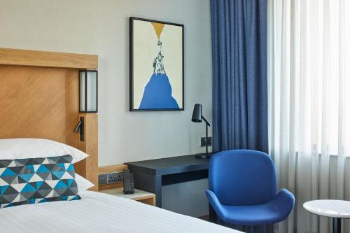 a bedroom with a bed and a blue chair and a desk at Courtyard by Marriott Exeter Sandy Park in Exeter