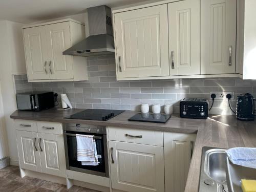 uma cozinha com armários brancos e um forno com placa de fogão em Mews Cottage em Appleby
