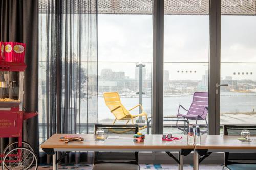 a room with three chairs and tables and windows at Moxy Amsterdam Houthavens in Amsterdam