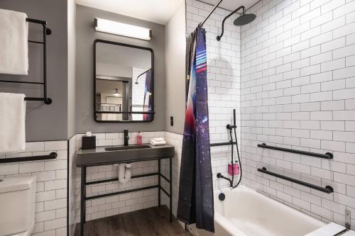 a bathroom with a sink and a tub and a mirror at Moxy Nashville Vanderbilt Area in Nashville