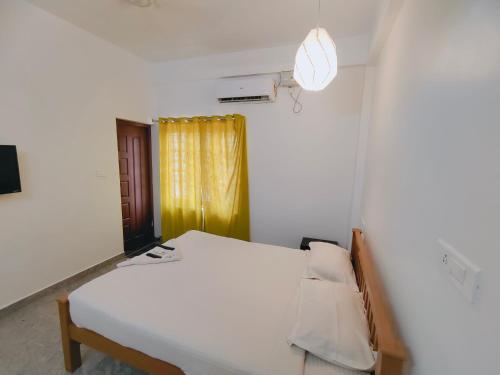 a bedroom with a white bed and a yellow curtain at Retaj Residency in Ernakulam