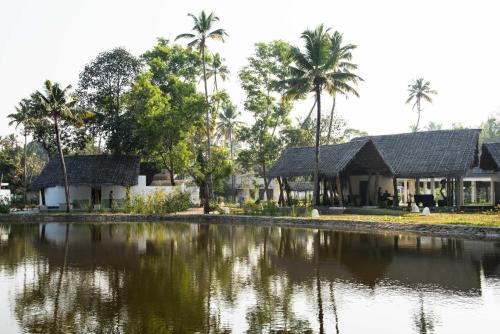a house with palm trees and a body of water at Xandari Pearl Beach Resort in Mararikulam