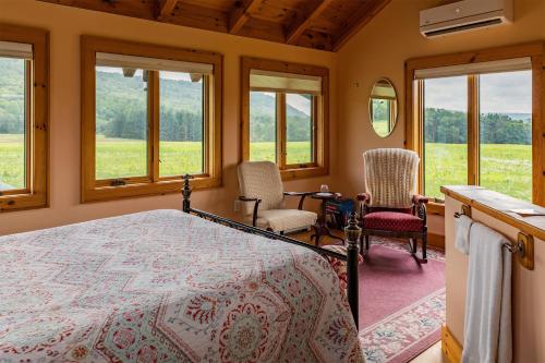 a bedroom with a bed and two chairs and windows at Tenwood Lodge in Ithaca