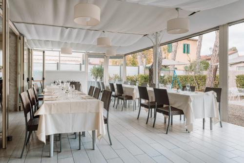 un ristorante con tavoli e sedie bianchi e finestre di Hotel Milton a Marina di Pietrasanta