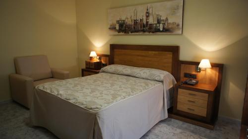 a bedroom with a bed and a chair and two lamps at Hotel Puente Romano in Alcántara