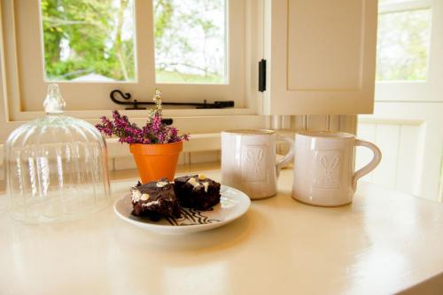 una mesa con un plato de pastel de chocolate y dos tazas en The Snug, Netherby, near Carlisle, en Longtown