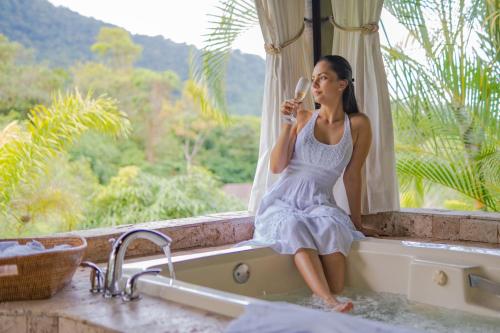 a woman sitting in a bath tub looking out a window at Hotel Lomas del Volcan in Fortuna