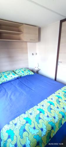a bedroom with a bed with a blue and white comforter at Mobil home 2 chambres tout équipé in Hourtin