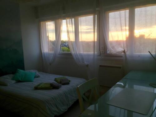 Schlafzimmer mit einem Bett, einem Tisch und Fenstern in der Unterkunft Cozy'Maisonnette in Guipavas