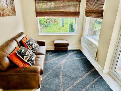 a living room with a leather couch and two windows at Spacious & modern 3 bedroom house in Peterlee in Wingate