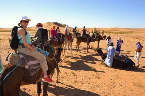 Un gruppo di persone che cavalcano cammelli nel deserto di Camp Mbark authentic a Mhamid