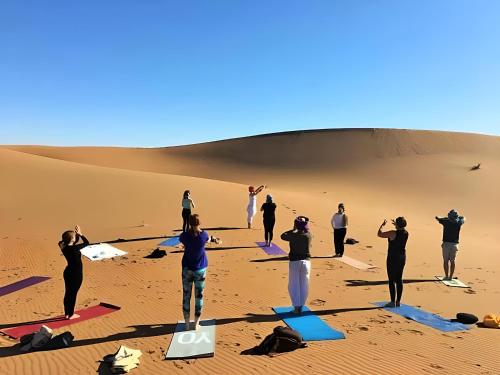 a group of people doing yoga in the desert at Camp Mbark authentic in Mhamid
