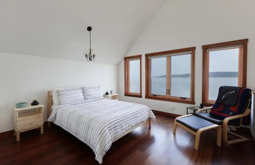 a bedroom with a bed and a chair and windows at WhidbeyBeachHouse, an Oceanfront Getaway on a Private Beach in Langley