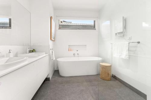Baño blanco con bañera y lavamanos en Pukeko Beach House en Rhyll