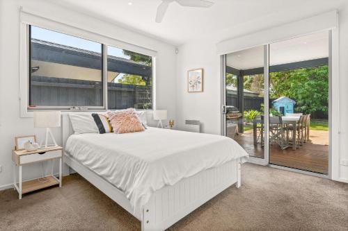 Dormitorio blanco con cama y ventana grande en Pukeko Beach House en Rhyll