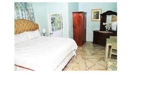 a bedroom with a large white bed and a dresser at Dela de-Rose Guest House Negril Jamaica in Negril