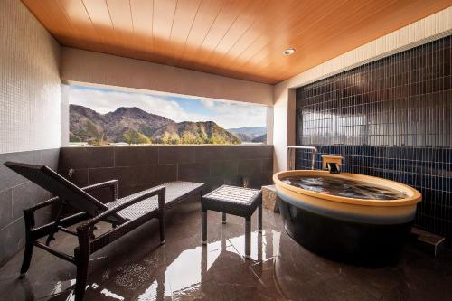 a bathroom with a tub and a view of mountains at Kawaguchiya Kinosaki Riverside Hotel in Toyooka