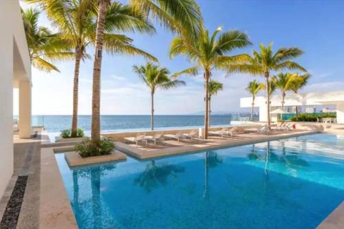 a swimming pool with palm trees and the ocean at Beachfront & free daily breakfast & 600MB 7010 Wifi by Moikkarentals in Puerto Vallarta