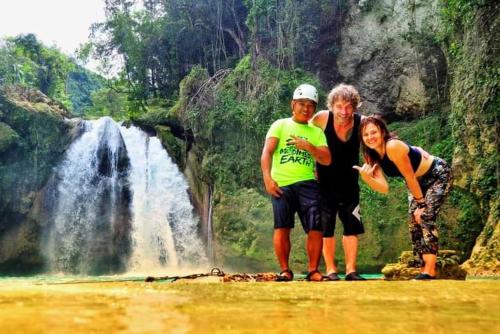 three people standing in front of a waterfall at House of TamSe Laagans ' Inn in Badian