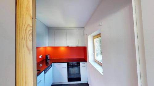 une cuisine avec des placards blancs et un mur rouge dans l'établissement Apartment Piz Cotschen, à Pontresina