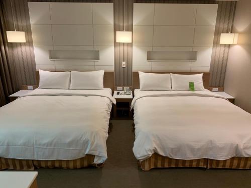 um quarto de hotel com duas camas com lençóis brancos em Kindness Hotel - Sandou II em Kaohsiung