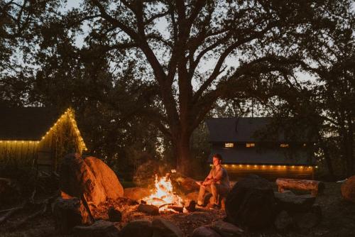 un homme assis autour d'un feu de camp la nuit dans l'établissement Lovers nest by Casa Oso with private hiking trails and pond, à Mariposa