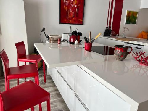une cuisine avec un comptoir blanc et des chaises rouges dans l'établissement Une pause…au soleil Classé 4 étoiles 108 m2 à 3min à pieds de la plage, à La Grande Motte