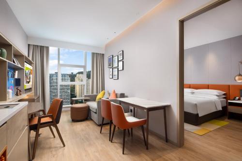 重慶市にあるHome2 Suites by Hilton Chongqing Yubeiのベッド、テーブル、椅子が備わるホテルルームです。