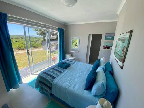 1 dormitorio con cama azul y ventana grande en Grys Patrys - 4 Beds Beach Home, en Jeffreys Bay