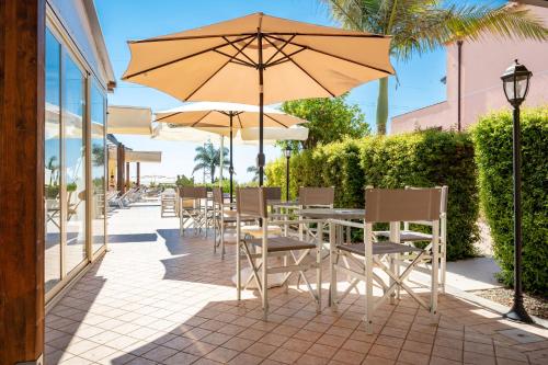 una mesa y sillas con una sombrilla en el patio en La Terra Dei Sogni Country Hotel en Fiumefreddo di Sicilia