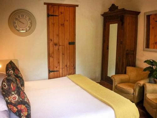 a bedroom with a bed and a chair and a clock at The Oil Mill Guesthouse in Swellendam
