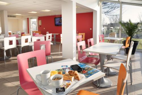 a cafeteria with white tables and pink chairs and food at Premiere Classe Maubeuge in Feignies