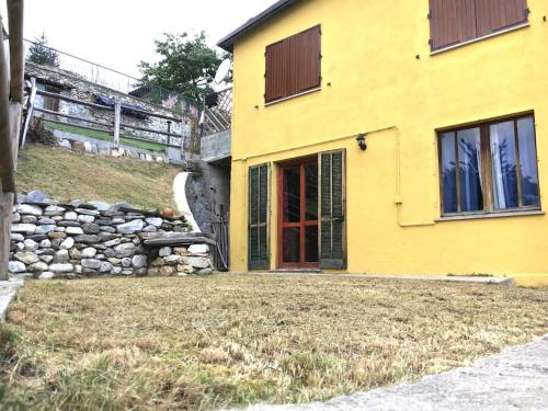 une maison jaune avec un mur en pierre et une porte rouge dans l'établissement Accogliente appartamento in centro, à Frabosa Soprana