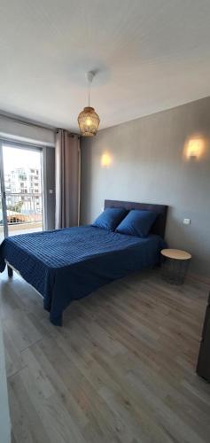 Schlafzimmer mit einem Bett mit blauer Bettwäsche und einem Fenster in der Unterkunft Charmant 2 pièces balcon vue mer in Vallauris