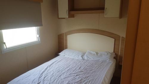 a small bedroom with a bed with white sheets and a window at 22 Kestrel quays in Flamborough
