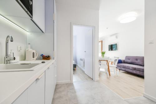eine weiße Küche mit einem Waschbecken und ein Wohnzimmer in der Unterkunft Słońce & Plaża Apartamenty Krynica Morska w Nautikka Park in Krynica Morska