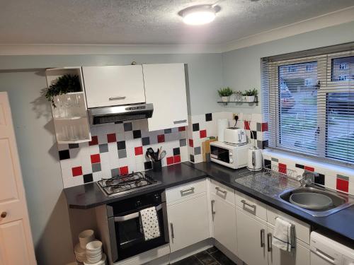 una cocina con armarios blancos y azulejos rojos y blancos en la pared en Rent Unique the Beeches 2bed, en Crawley