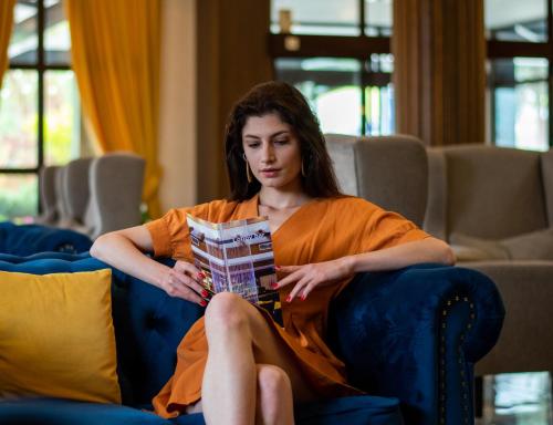a woman sitting on a couch reading a book at Grand Hotel Velingrad in Velingrad