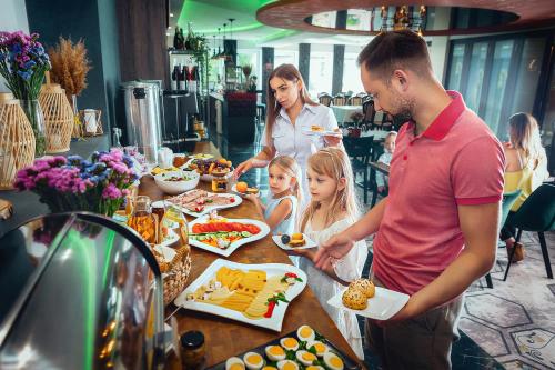 Een man, een vrouw en twee kinderen bereiden eten voor bij een buffet. bij Zacisze Nad Nidą Resort in Pińczów