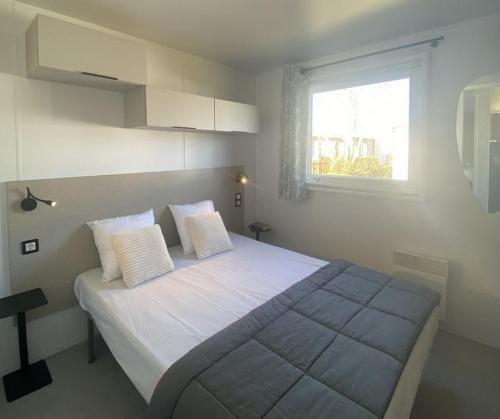1 dormitorio con 1 cama con sábanas blancas y ventana en Camping de Keranterec, en La Forêt-Fouesnant
