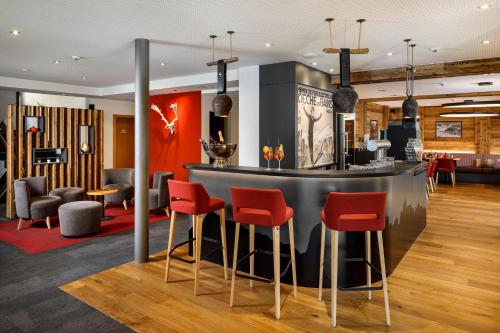 a bar in a hotel lobby with red chairs at Therme 51° Hotel Physio & Spa in Leukerbad