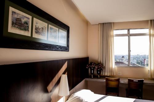 a hotel room with a bed and a desk and a window at Pousada Sossego da Pampulha in Belo Horizonte
