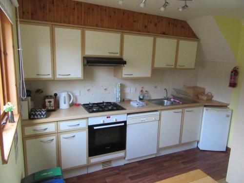 a kitchen with white cabinets and a stove and a sink at Osprey, Longhouse Cottages in Rosemarkie