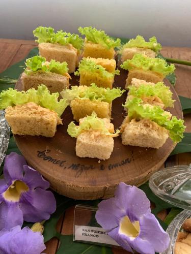 a group of sandwiches on a wooden plate with purple flowers at Pousada Cheiro de Mato in Bonito