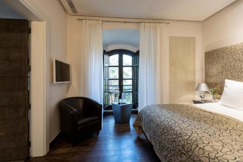 a bedroom with a bed and a chair and a window at Hospes Palacio del Bailio, a Member of Design Hotels in Córdoba